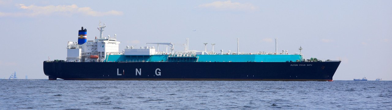 The LNG carrier Puteri Firus Satu passes through Tokyo Bay with its dark-blue hull and pale-green deck tanks visible.